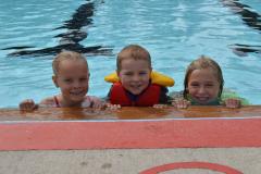 Three kids post at the edge of a swimming pool